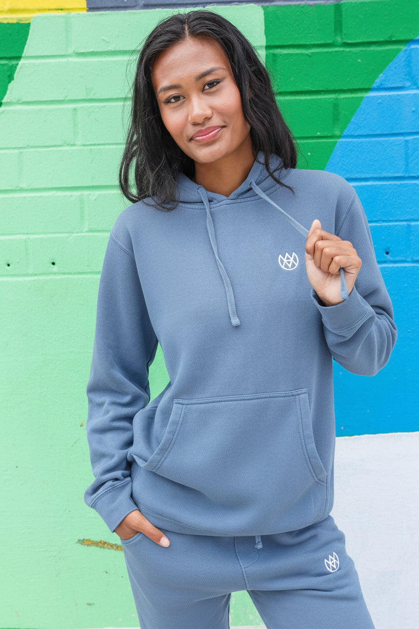 Person wearing a blue hoodie and pants with a logo against a colorful wall.