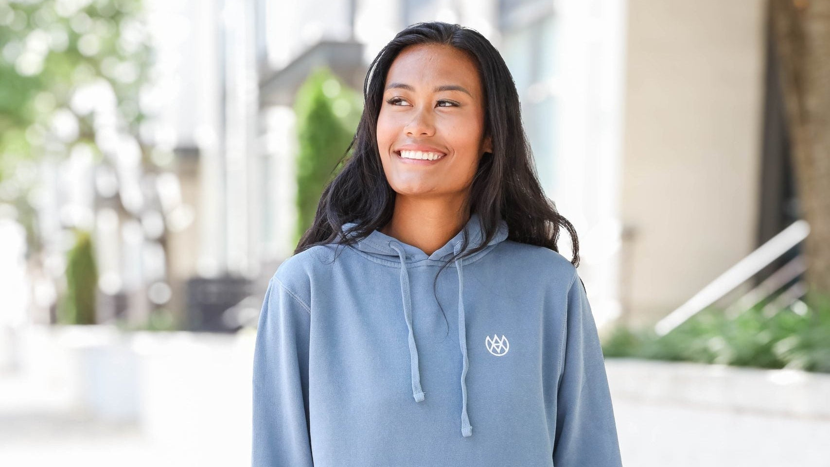Woman wearing a blue hoodie with a logo, standing outdoors.