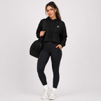 Woman wearing a black hoodie and leggings with a duffel bag on a white background