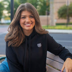 Woman wearing a black hoodie with a logo, sitting on a bench outdoors.