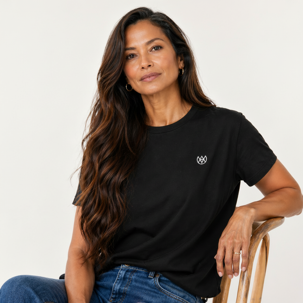 Woman wearing a black t-shirt with a small logo, sitting on a chair against a plain background