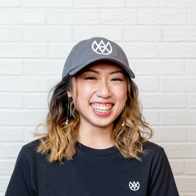 Person wearing a cap and black shirt with a logo, standing against a textured wall.