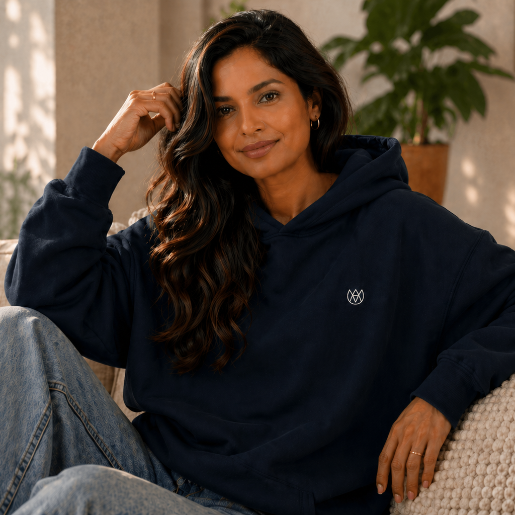 Woman wearing a navy blue hoodie with a logo, sitting on a couch in a cozy living room.